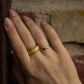 Woman’s hand wearing maple burl ring, resting against textured brick wall in soft natural light.