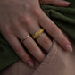 Close-up of hand with maple burl wood ring and gold accents, resting on green fabric for soft contrast.