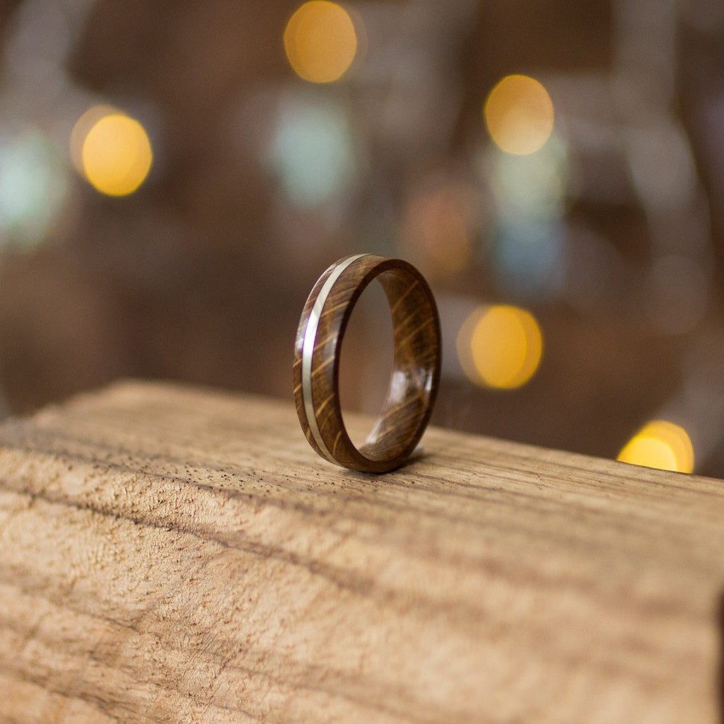 Angled close-up of oak wood ring with silver stripe, showing curved grain texture and soft light reflections.