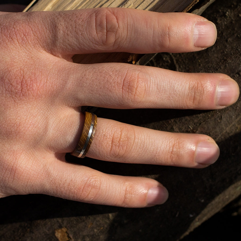 Close-up of fingers wearing oak wood ring with silver inlay, highlighting natural wood tones against skin.